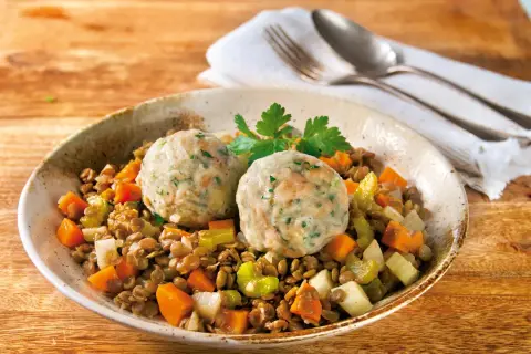Zwei Semmelknödel auf Linsengemüse mit Karotten und Sellerie, garniert mit Petersilie.