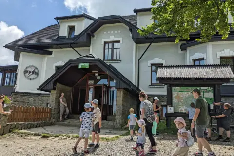 Rodzina przy schronisku na Magurce Wilkowickiej. Dzieci zwiedzają okolicę, a dorośli planują trasę na mapie.