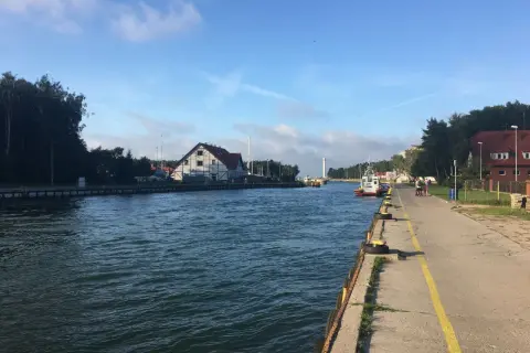 Spacerem nad jeziorem Sarbsko, widać kanał, budynki i łodzie.