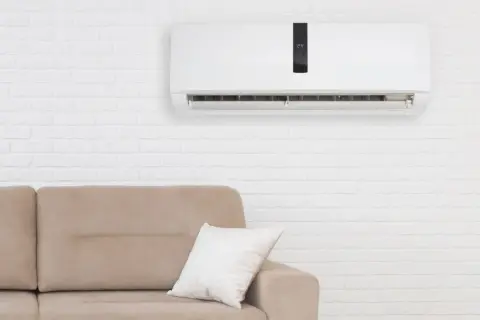 Condizionatore senza motore esterno come funziona: un'unità bianca a parete sopra un divano beige, con un display digitale che mostra 24 gradi.