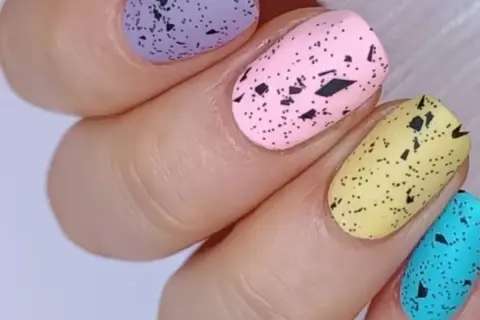 Delikatne, **milky nails** w pastelowych kolorach: fioletowym, różowym, żółtym i turkusowym, ozdobione czarnymi plamkami imitującymi skorupki jajek.