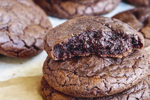 En hög med kladdkake cookies, en är uppäten och visar den sega, chokladiga insidan. Perfekt för fikat!