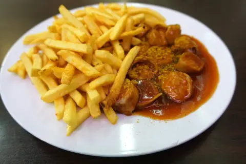 Eine Portion knuspriger Pommes Frites neben einer Currywurst in würziger Sauce, ein Klassiker aus Berlin.