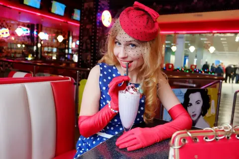 Kobieta w stylu pin up pije mleczny koktajl w retro restauracji.