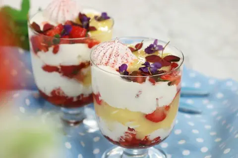 Två glas med Eton Mess, lager av vispad grädde, jordgubbar och maräng, toppade med blommor.