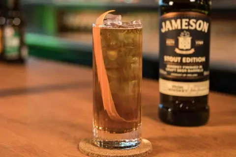 Orzeźwiający drink z whisky Jameson Stout Edition, lodem i skórką pomarańczy. Idealny na wieczór.