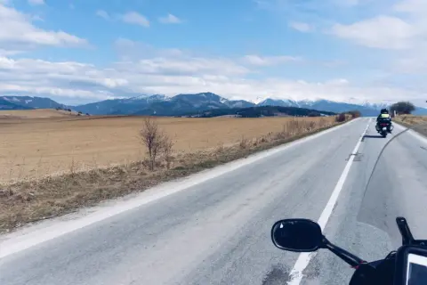 Motocykliści jadący drogą w kierunku ośnieżonych gór Tatr.