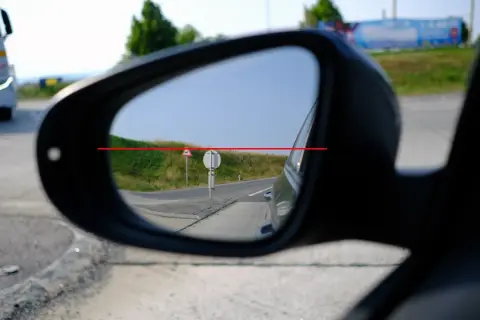 Blick in den Rückspiegel: Ein LKW fährt vorbei. Die rote Linie zeigt, wie man das Spiegelglas richtig einstellen kann, um die Straße im Blick zu behalten.