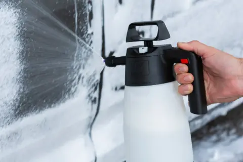 Mano che spruzza schiuma per lavare auto a casa con un'idropulitrice.