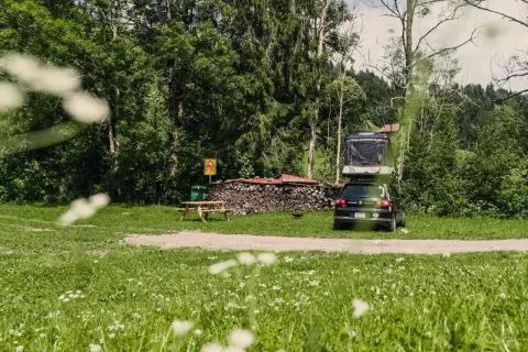 Campingplatz mit Dachzeltauto, Holzstapel und Picknicktisch. Ein idyllischer Ort für Basel Geheimtipps abseits des Trubels.