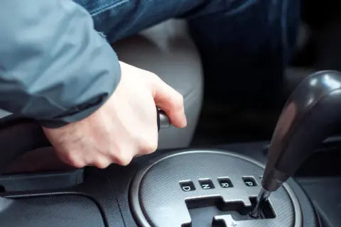 Main d'un conducteur actionnant le frein à main dans une voiture, prêt à démarrer.