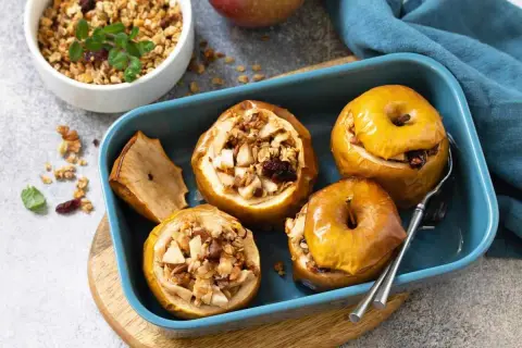 Mele cotte ripiene di frutta secca e granola, servite in una teglia blu.