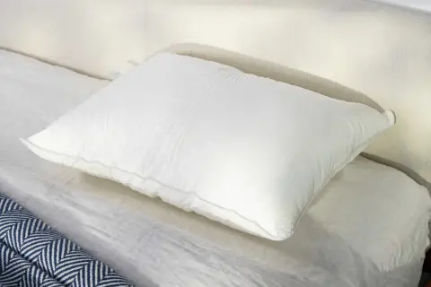 A plush white pillow rests on a neatly made bed, perfect for a comfortable night's sleep, especially for those who prefer to sleep on their stomach.