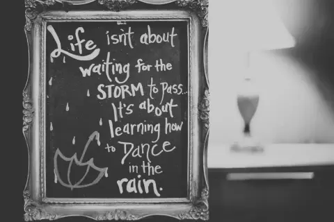 Czarno-biała tablica w ozdobnej ramie z inspirującymi cytatami po angielsku: "Life isn't about waiting for the storm to pass. It's about learning how to dance in the rain.
