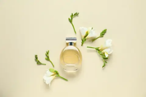 Elegancka butelka perfum otoczona delikatnymi kwiatami frezji. Zapach frezji unosi się w powietrzu, tworząc subtelną kompozycję.