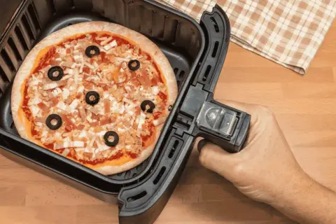 Une pizza garnie d'olives noires et de fromage est prête à être cuite dans un airfryer.