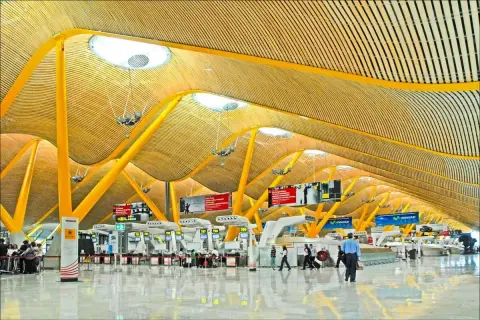 Nowoczesna architektura lotniska Madryt Barajas z żółtymi podporami i drewnianym sufitem.