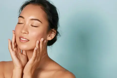 Donna con pelle luminosa e mani sul viso, un esempio di perché i coreani hanno la pelle perfetta.