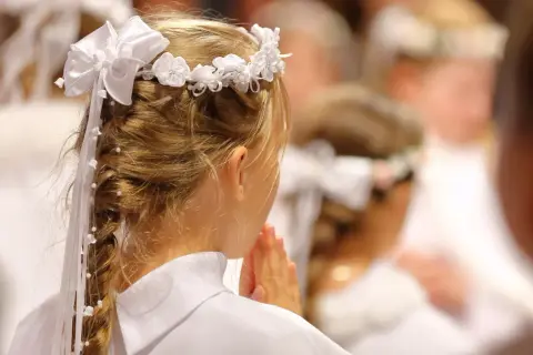 Dziewczynka w białej sukience i wianku modli się. To piękny widok, co na komunie.