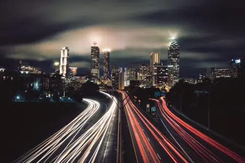 Nocne miasto w technice time lapse. Smugi świateł samochodów na autostradzie przed oświetlonymi wieżowcami.