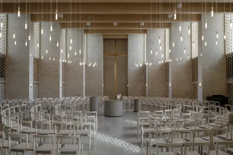 Innenraum einer modernen Kirche mit Reihen von Holzbänken, einem goldenen Kreuz und vielen hängenden Lichtern.