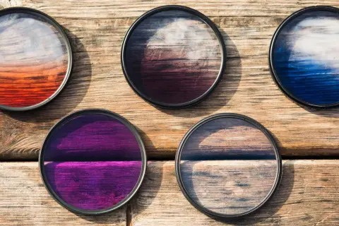 Five circular camera filters with colorful gradients, perfect for telephoto photography, lie on a wooden surface.