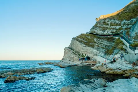 Scogliere rocciose e mare blu intenso al Conero, con un tunnel scavato nella roccia e persone che si godono la giornata.