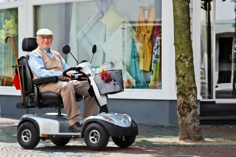 Älterer Herr im elektrischen Rollstuhl vor einem Schaufenster. Dank der Krankenkasse kann er mobil bleiben.