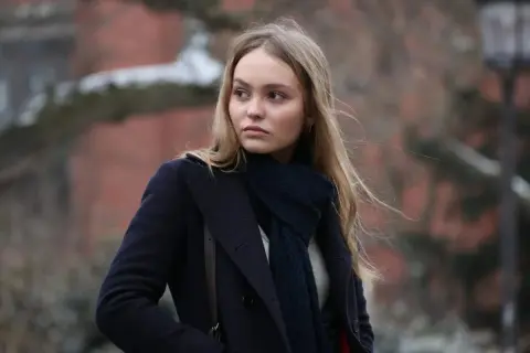Lily-Rose Depp i en mörkblå kappa och halsduk, påminner om hennes roller i filmer.