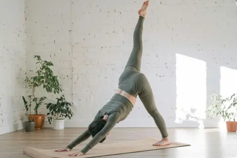 Mujer en postura de yoga de tres patas, explorando el vinyasa significado. El flujo dinámico se refleja en su movimiento.