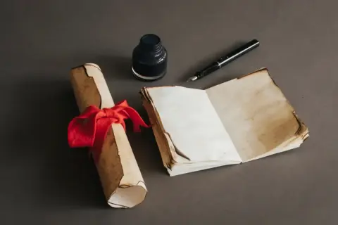 Zrolowany dokument z czerwoną wstążką, otwarta księga i kałamarz z piórem. Może to być inspiracja do napisania piosenki na 3 maja.