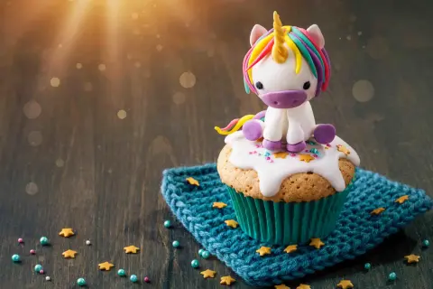 Un cupcake orné d'un adorable licorne en pâte à sucre, posé sur un glaçage blanc et des étoiles dorées. Le glaçage cupcake sucre glace est parfait pour une touche magique.