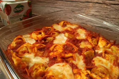 Pyszna zapiekanka z tortellini w sosie pomidorowym, zapieczona z serem. Obok kartonik przecieru pomidorowego Łowicz.
