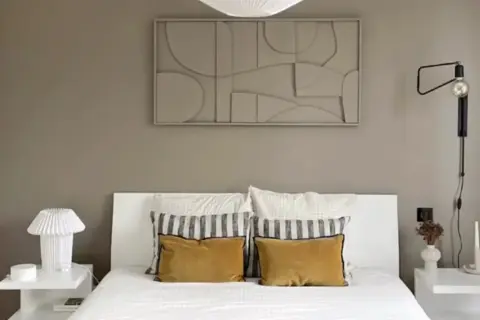 Une chambre moderne avec un lit blanc, des coussins moutarde et un tableau abstrait. Une belle idée tableau créatif pour une décoration murale apaisante.
