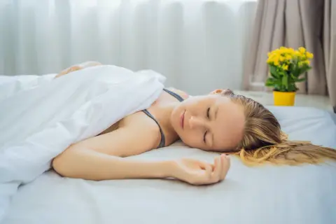 A woman sleeps peacefully on a white bed, her head resting directly on the mattress. Is it better to sleep without a pillow?