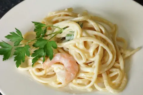 Cremige Pasta al Limone mit Garnelen und Petersilie auf einem weißen Teller. Ein Genuss für Augen und Gaumen.