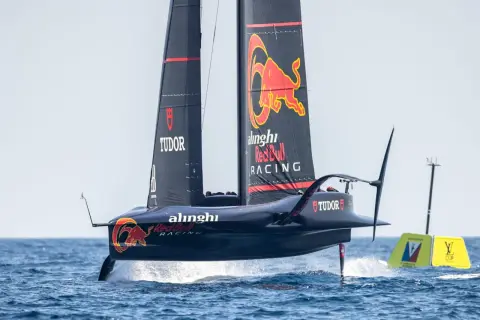 Wyścigowy jacht klasy AC75 z logo Red Bull Racing i Alinghi, unoszący się nad wodą na foilach.