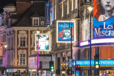 Nocne światła teatrów w londyńskim **West Endzie**: plakaty "Les Misérables", "The Crucible" i "2:22 A Ghost Story" oświetlają ulicę.