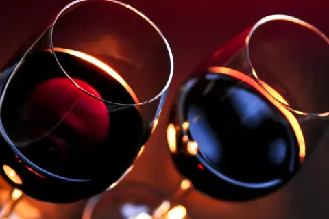 Dwa kieliszki z czerwonym winem, w blasku świec. Czy wino wytrawne jest zdrowe? Pytanie pozostaje otwarte.