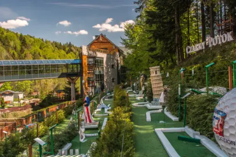Mini golf z atrakcjami jak Krzywa Wieża w Pizie i Statua Wolności, obok budynku i lasu.
