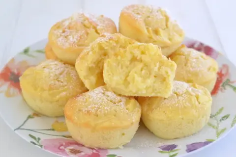Muffin alle mele soffici e dorati, cosparsi di zucchero a velo, su un piatto fiorito. Uno è tagliato a metà, mostrando la morbida consistenza.