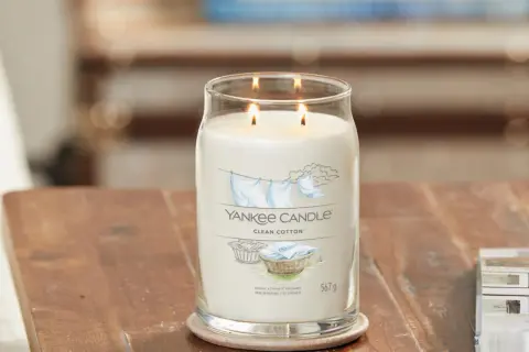 Zapalone świece zapachowe Yankee Candle Clean Cotton w szklanym słoju na drewnianym stole.