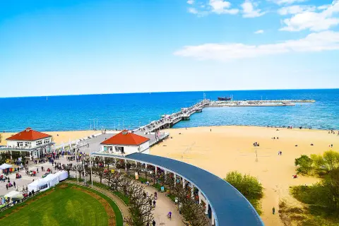 Słoneczna plaża w Sopocie z molo, budynkami i spacerującymi ludźmi.