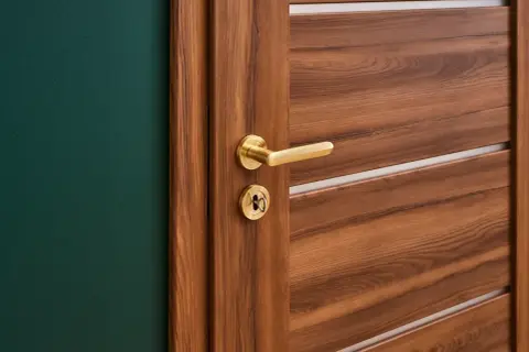 Nowe drzwi na stare futryny z Castoramy, z elegancką, złotą klamką i zamkiem, idealnie komponują się z zieloną ścianą.