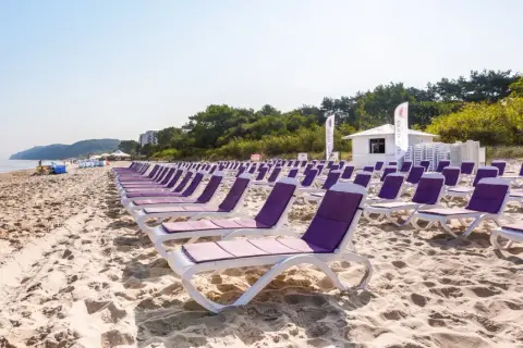 Rzędy leżaków na piaszczystej plaży, idealne na tanie wczasy nad morzem dla 2 osób. W tle morze i zieleń.