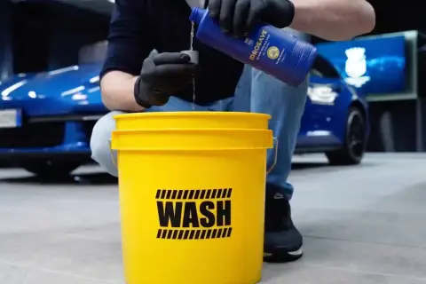 Przygotowanie do mycia samochodu na myjni: nalewanie płynu do wiadra z napisem "WASH".