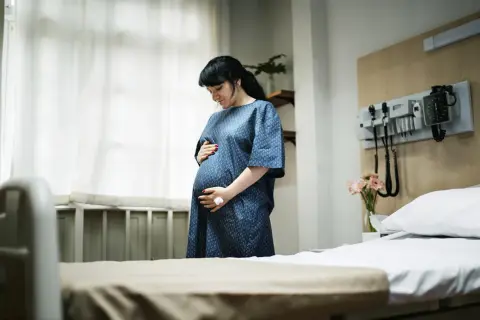 Kobieta w szpitalnej sali, trzymająca się za brzuch, szuka sposobów, jak złagodzić skurcze porodowe.