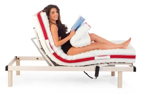 Donna sorridente legge un libro a letto, con il materasso regolabile che offre la postura corretta per guardare la TV o rilassarsi.