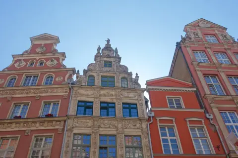 Bogata gdańsk architektura kamienic z detalami rzeźbiarskimi i ozdobnymi fasadami, widziana z dołu pod błękitnym niebem.