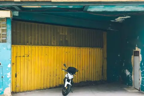 Moto aparcada frente a una cochera con puerta amarilla, se puede aparcar en una cochera sin vado.